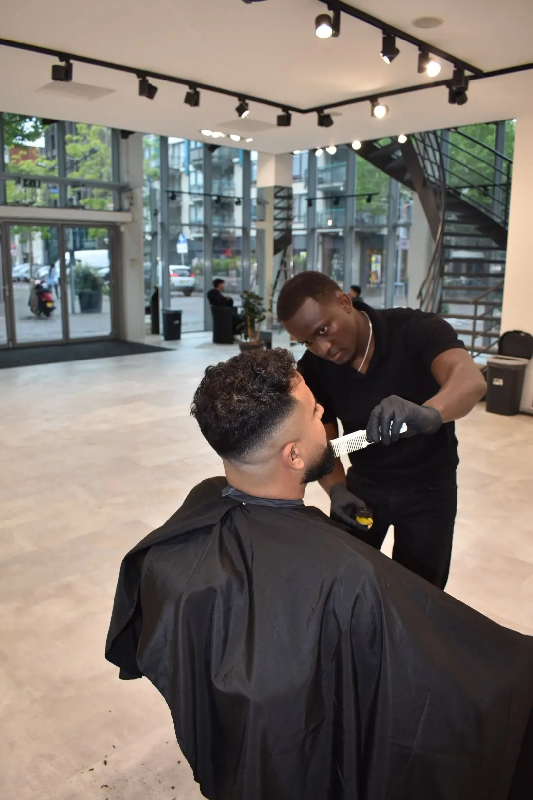 Barber werkt een fade bij, met de ramen van de studio op de achtergrond